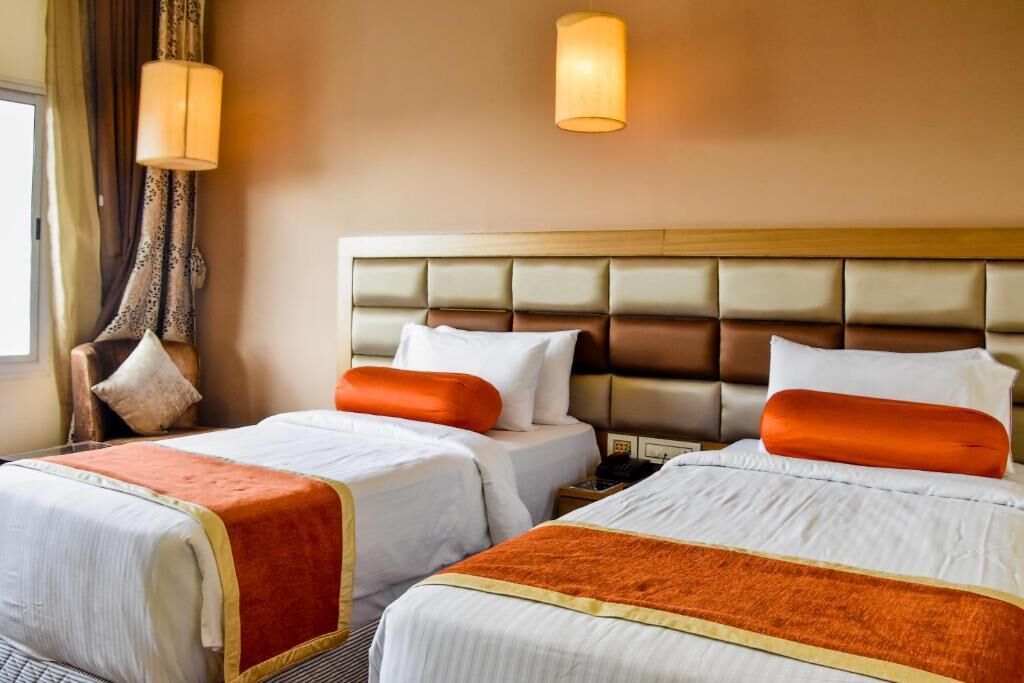 A hotel room with two beds, a headboard, and a nightstand.
