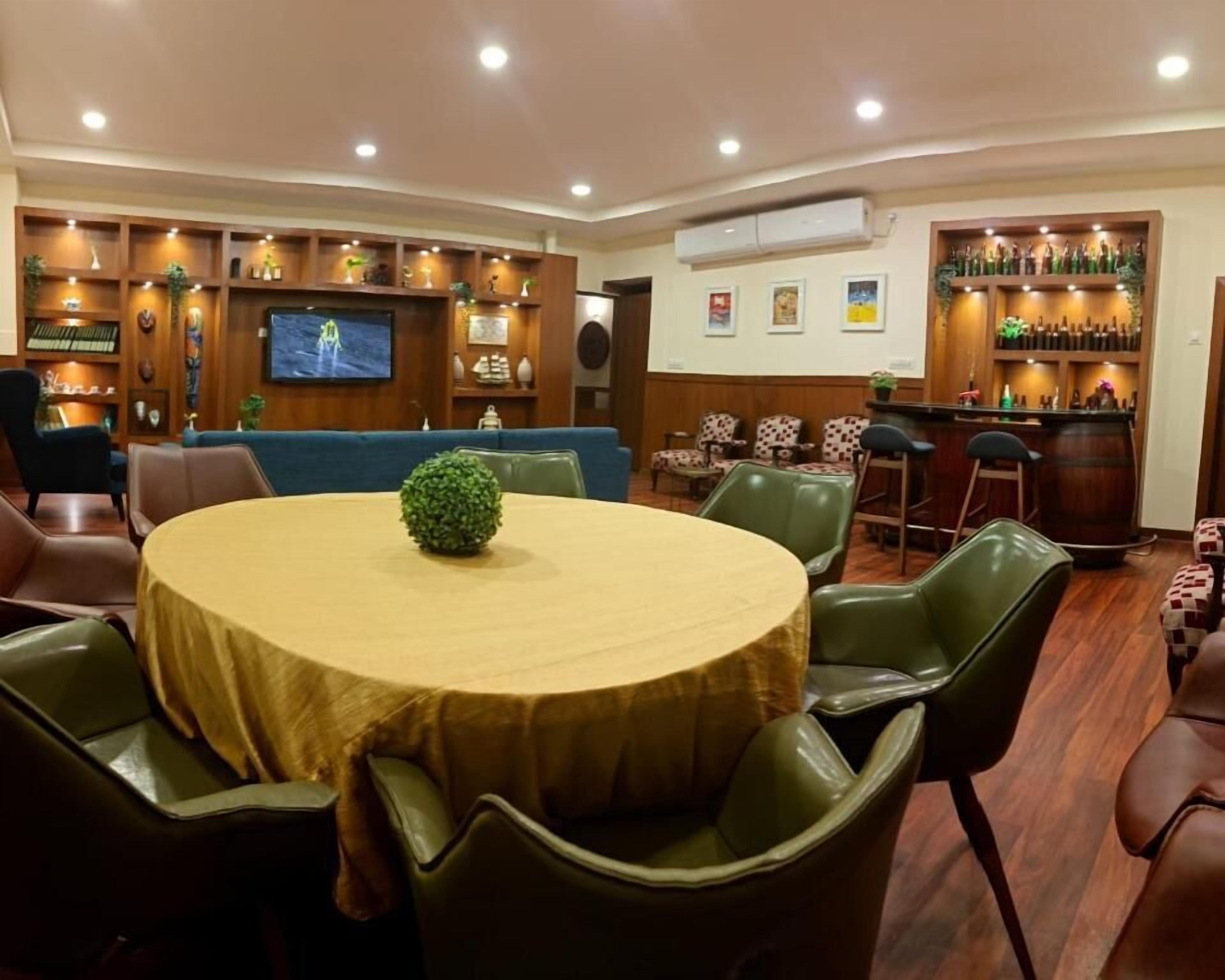 A dining area with a round table, green chairs, a television, and a bar area with shelves of bottles.