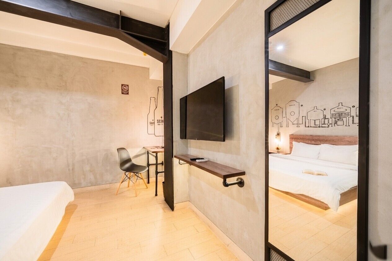 A hotel room with a bed, a desk, a chair, a TV mounted on the wall, and a bed with a book on it.