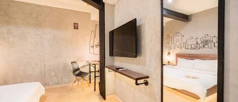 A hotel room with a bed, a desk, a chair, a TV mounted on the wall, and a bed with a book on it.