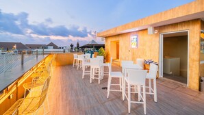 Un espace extérieur aménagé avec des chaises et des tables en osier blanc, une terrasse en bois et une vue sur le ciel.