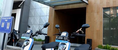 Duas scooters elétricas estacionadas em frente a um edifício com design moderno e uma placa indicando um hotel boutique.