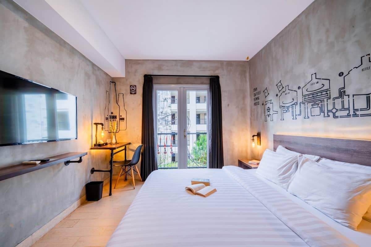 A modern hotel room with a large bed, a desk with a chair, a television, and a balcony with a city view.