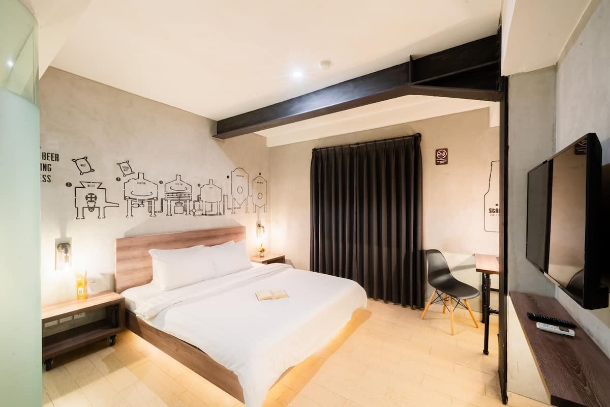 A hotel room with a large bed, a desk with a chair, a TV, and a wall mural.