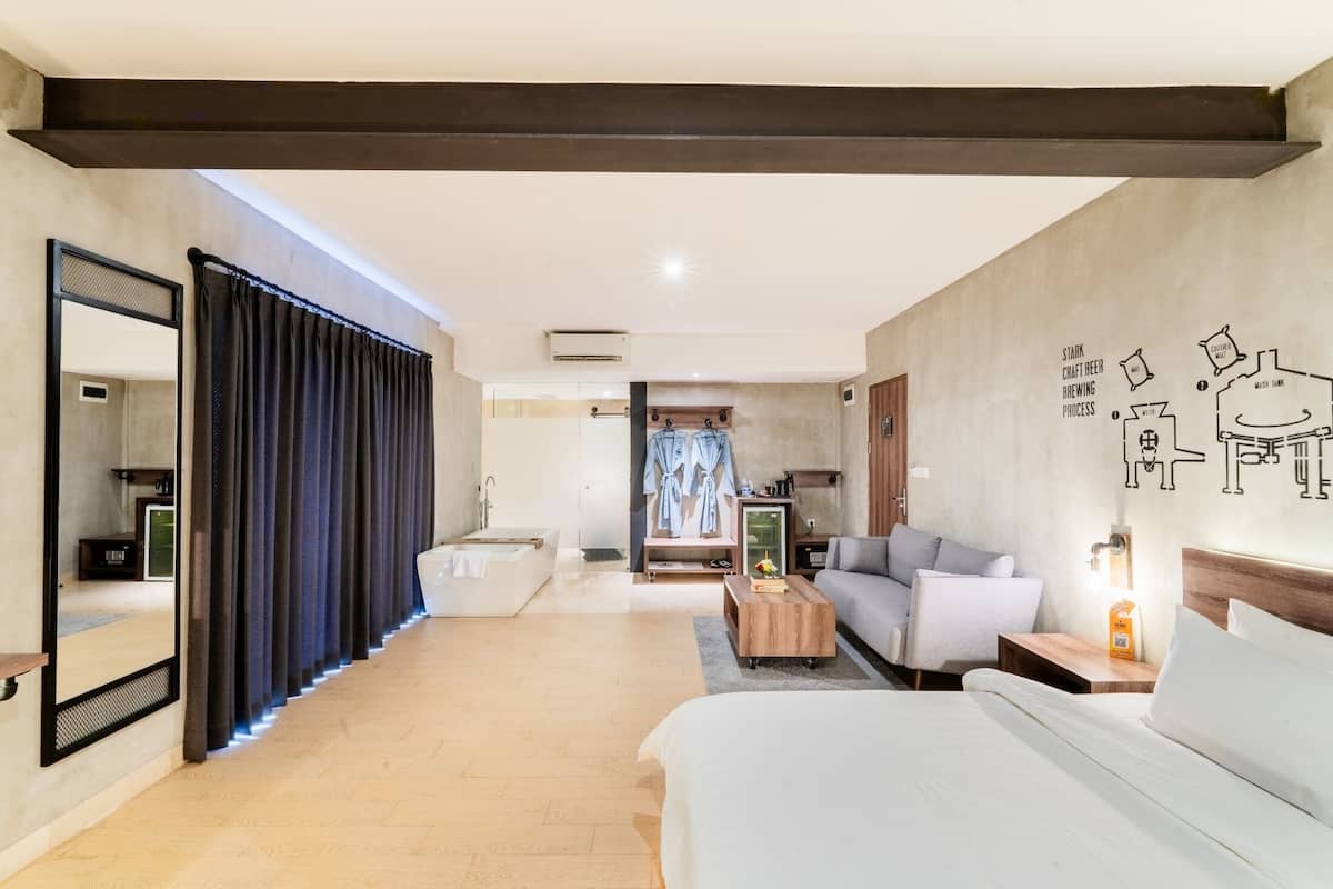 A modern hotel room with a large bed, a sofa, a coffee table, and a seating area with a view of the kitchen.