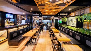 Un restaurant avec des tables et des bancs en bois, un coin bar et un mur végétal.