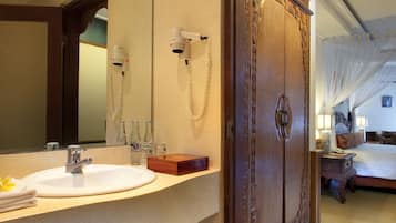 A bathroom with a sink, mirror, and vanity. There is a wooden door with intricate carvings and a small trash can.