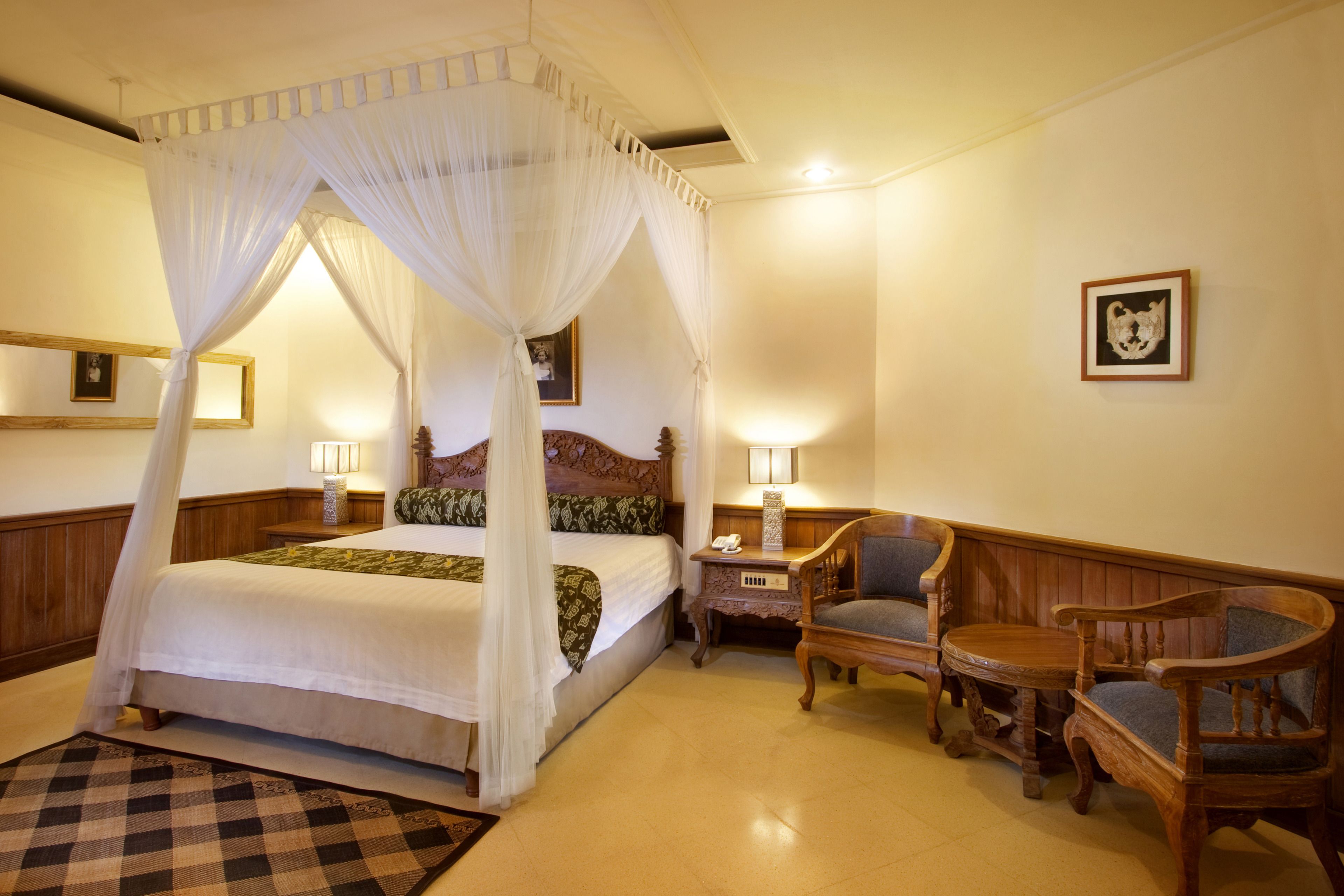 A four-poster canopy bed with a checkered rug, wooden furniture, and wall-mounted lamps.