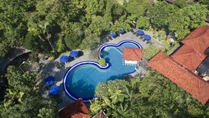 An aerial view of a resort with a central swimming pool, surrounded by lounge chairs and umbrellas, and lush greenery. - Matahari Bungalow (Kuta)