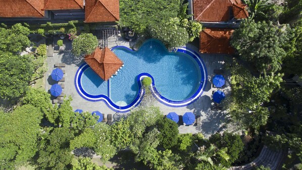 An aerial view of a resort with a large swimming pool, surrounded by lush greenery and shaded by umbrellas. - Matahari Bungalow (Kuta)
