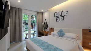 A modern hotel room with a large bed, a desk, and a view of the garden through the sliding glass door. - Matahari Bungalow (Kuta)