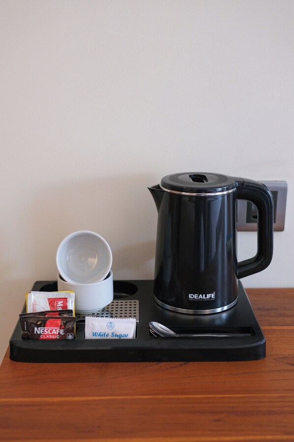 A black coffee maker, a white cup, a spoon, a Nescafe Classic packet, and a sachet of white sugar on a tray.