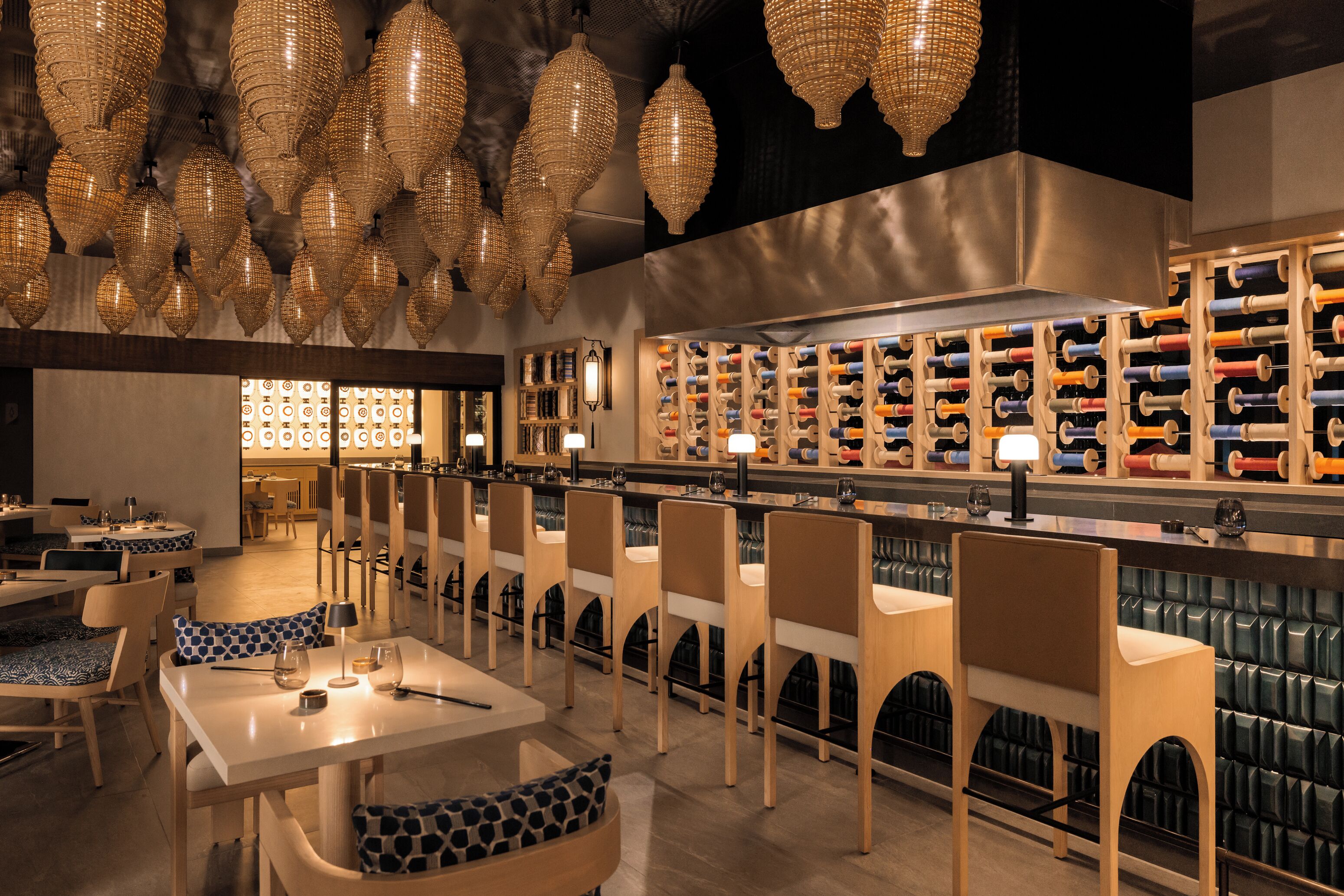 A restaurant with multiple tables and chairs, a bar area with a wine rack, and hanging decorative lights.