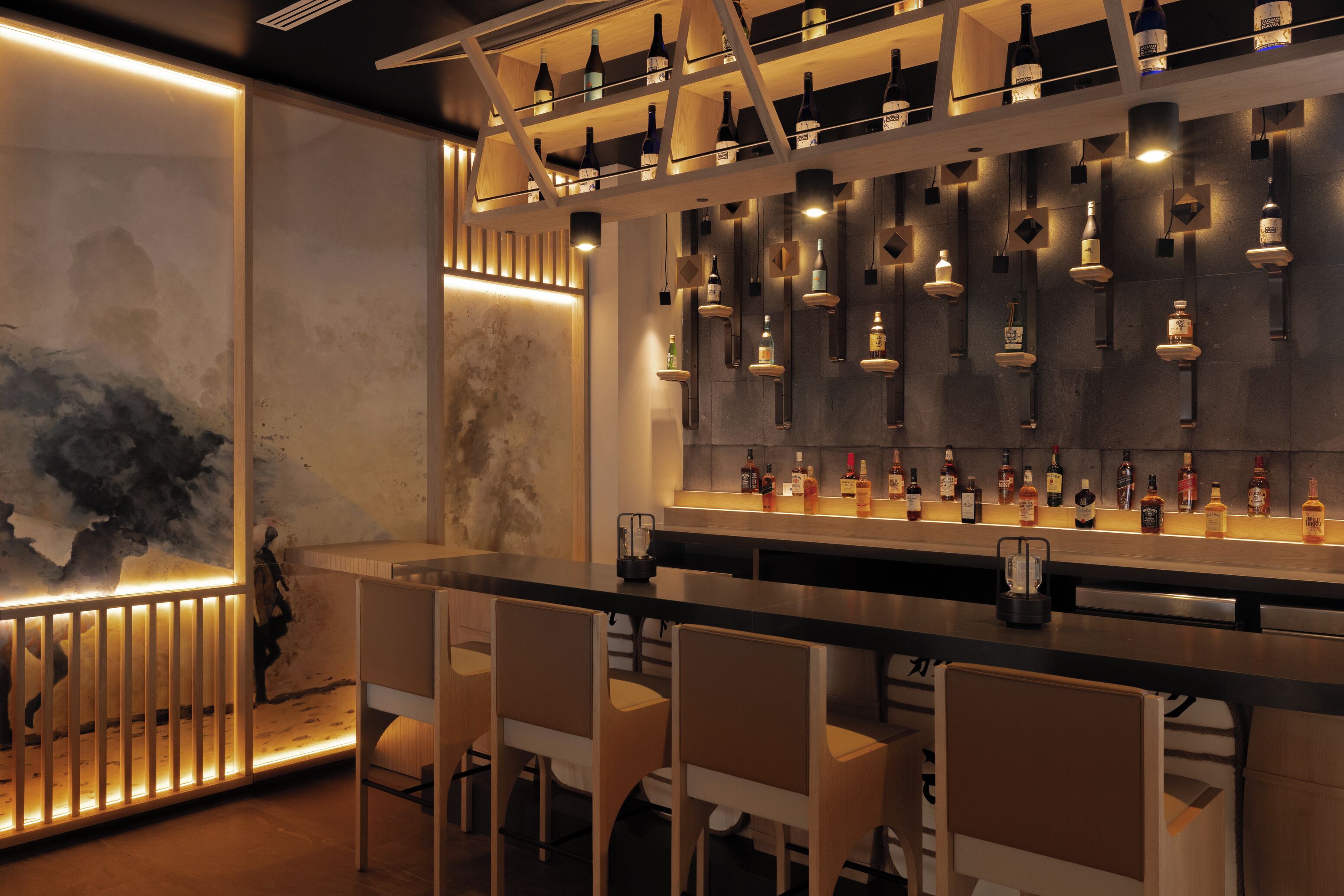 Un espace bar doté de plusieurs étagères remplies de bouteilles, de tabourets de bar et d’un mur orné d’œuvres d’art abstraites.