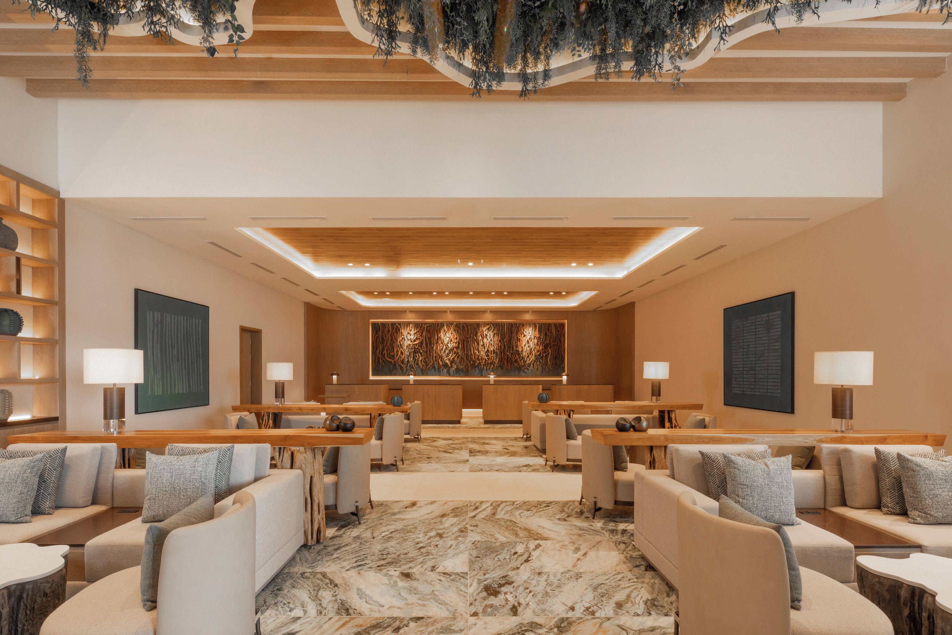 A hotel lobby with a central reception desk, seating areas, and a large abstract wall art piece.