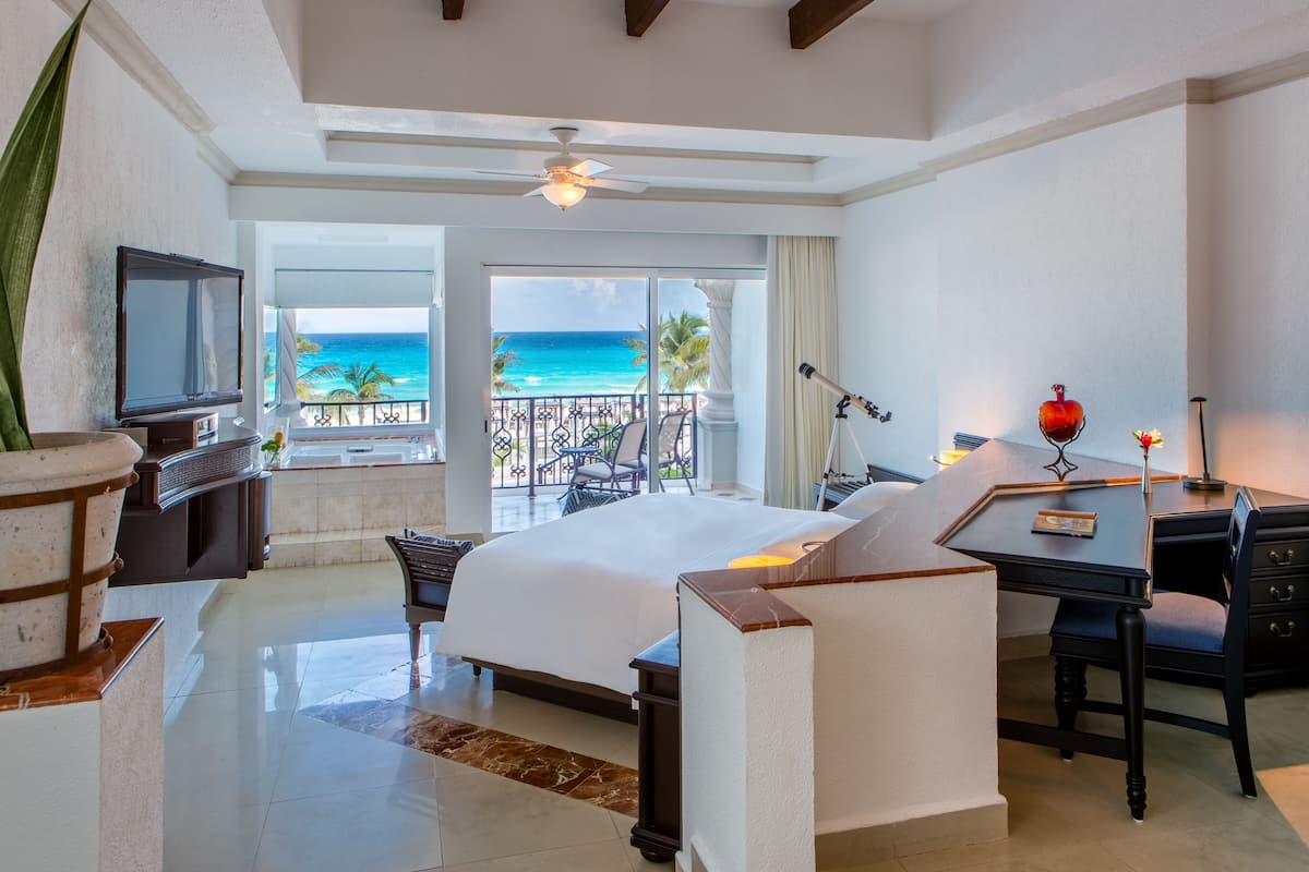 A hotel room with a bed, desk, and balcony with a view of the ocean.