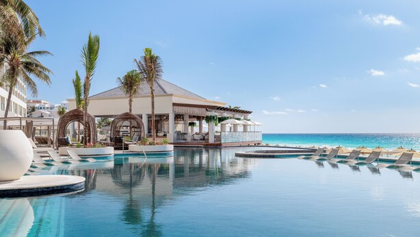 An infinity pool with lounge chairs, palm trees, and a building with a roofed area. - Hyatt Zilara Cancun   - Adults Only - All Inclusive (Cancun)