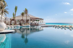 An infinity pool with lounge chairs, palm trees, and a building with a roofed area. - Hyatt Zilara Cancun   - Adults Only - All Inclusive (Cancun)