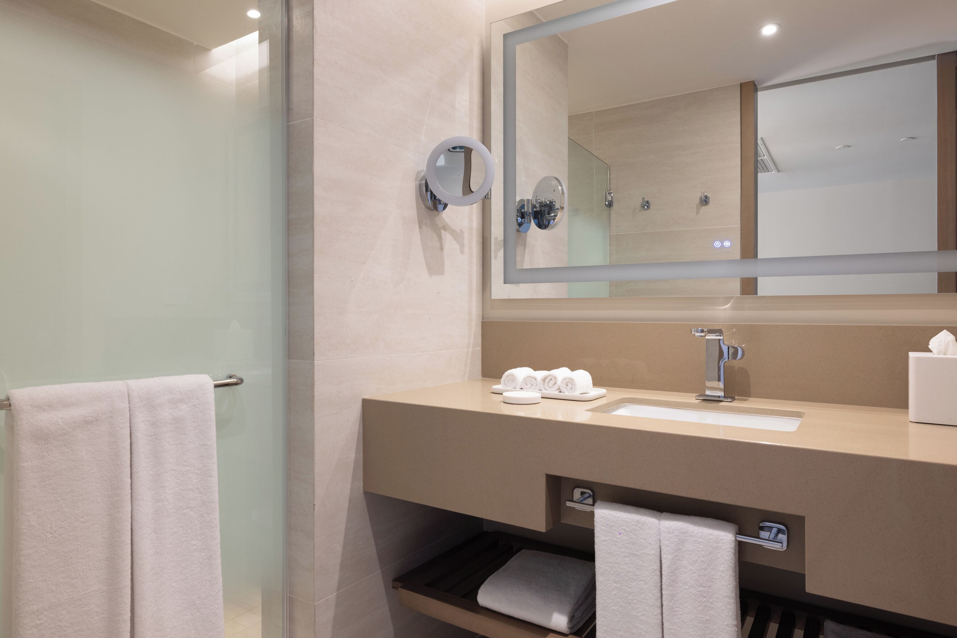 Un baño moderno con cabina de ducha de vidrio, un espejo grande y un mueble de tocador con lavabo y toallero.