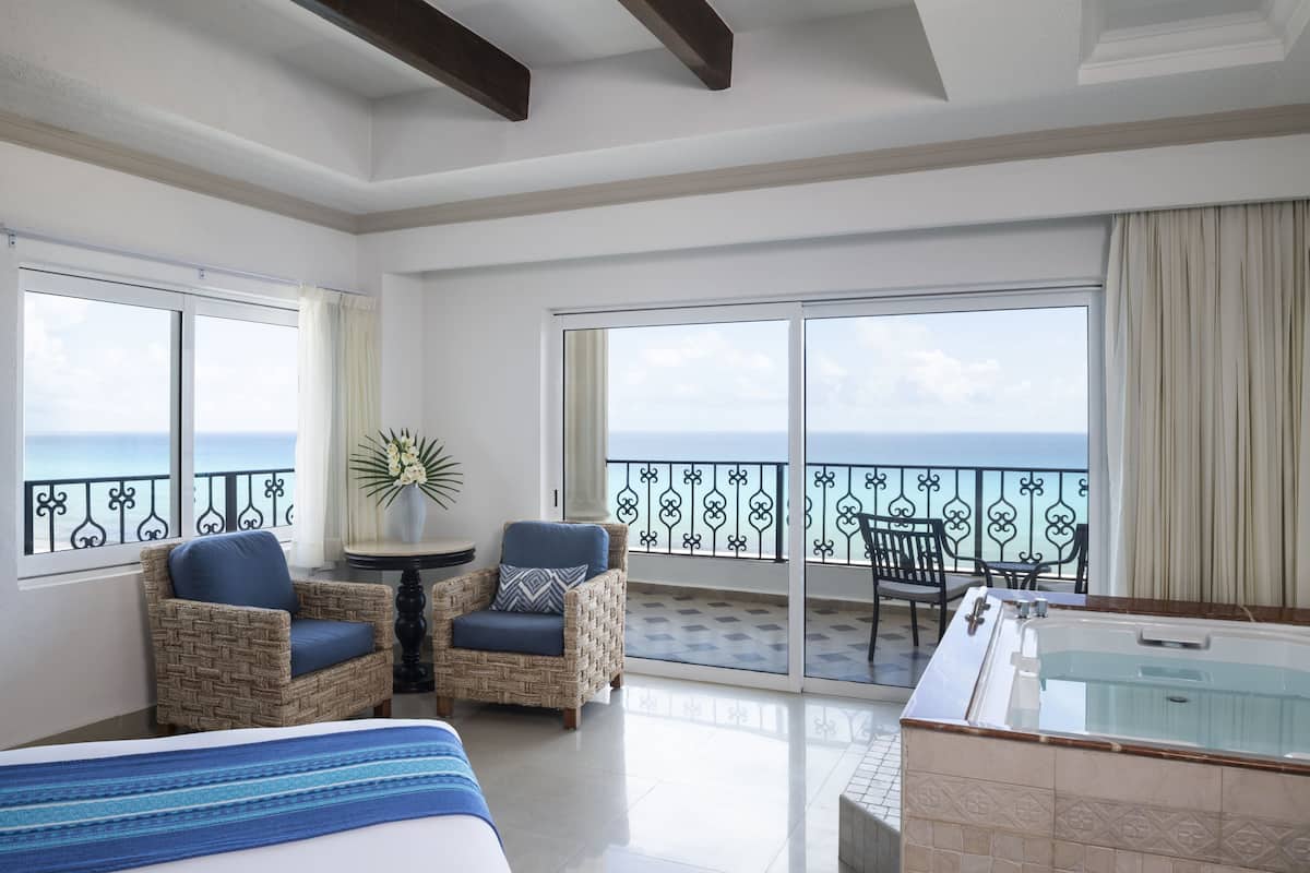 A balcony with a view of the sea, wicker chairs, a table, and a hot tub.