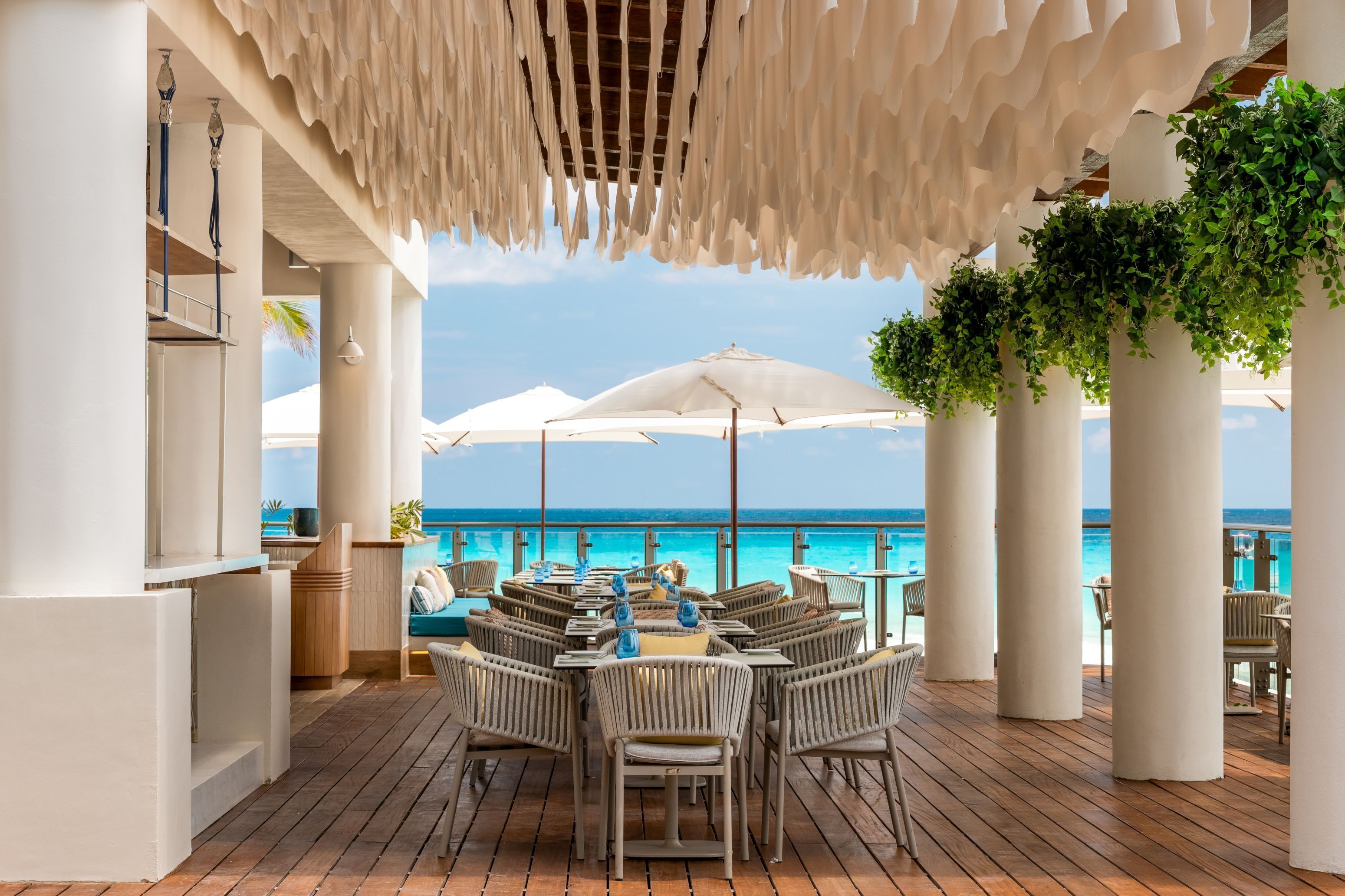 A covered outdoor seating area with tables and chairs, overlooking a pool and the ocean.