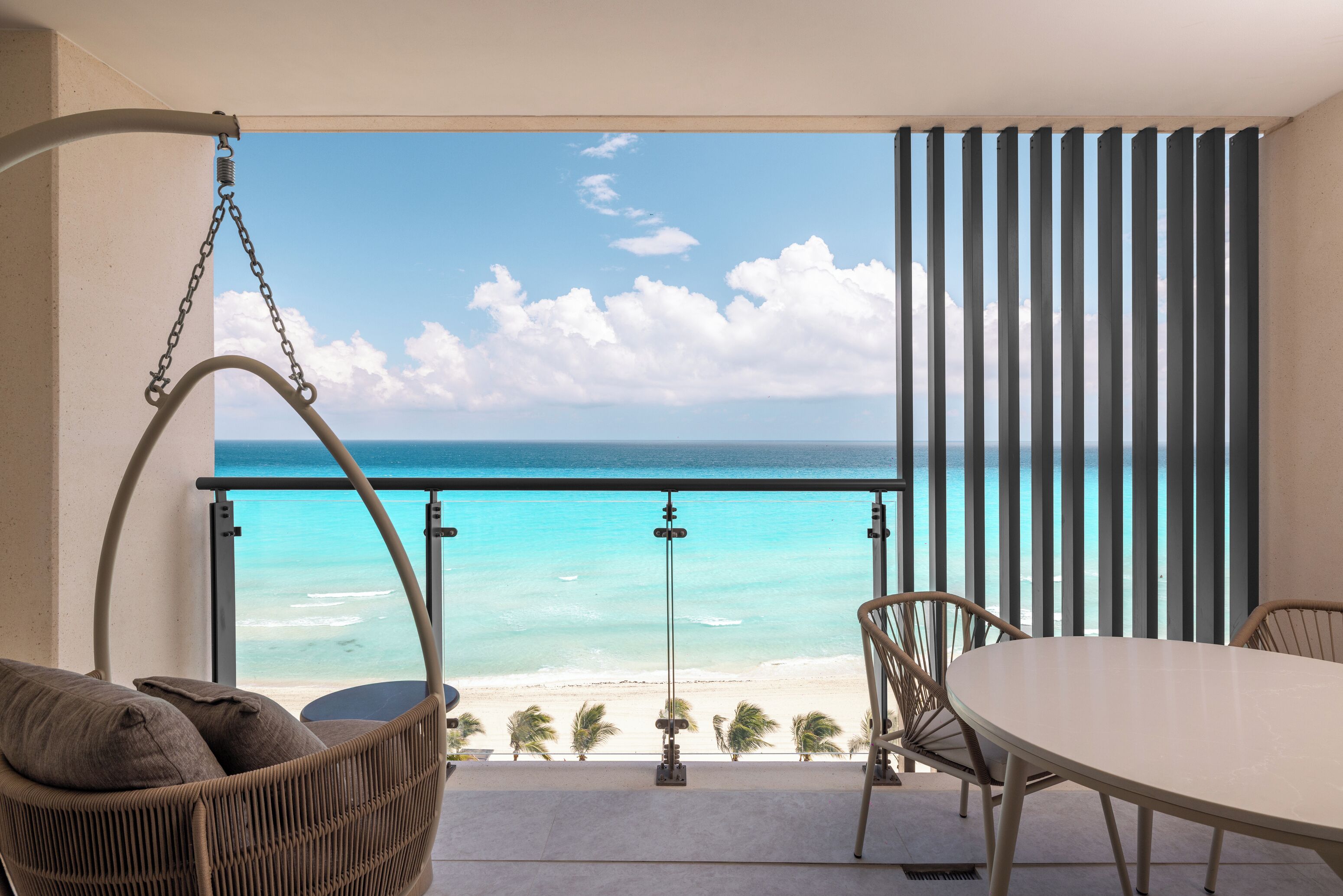 A balcony with a view of the ocean, a hanging chair, a table, and a chair.
