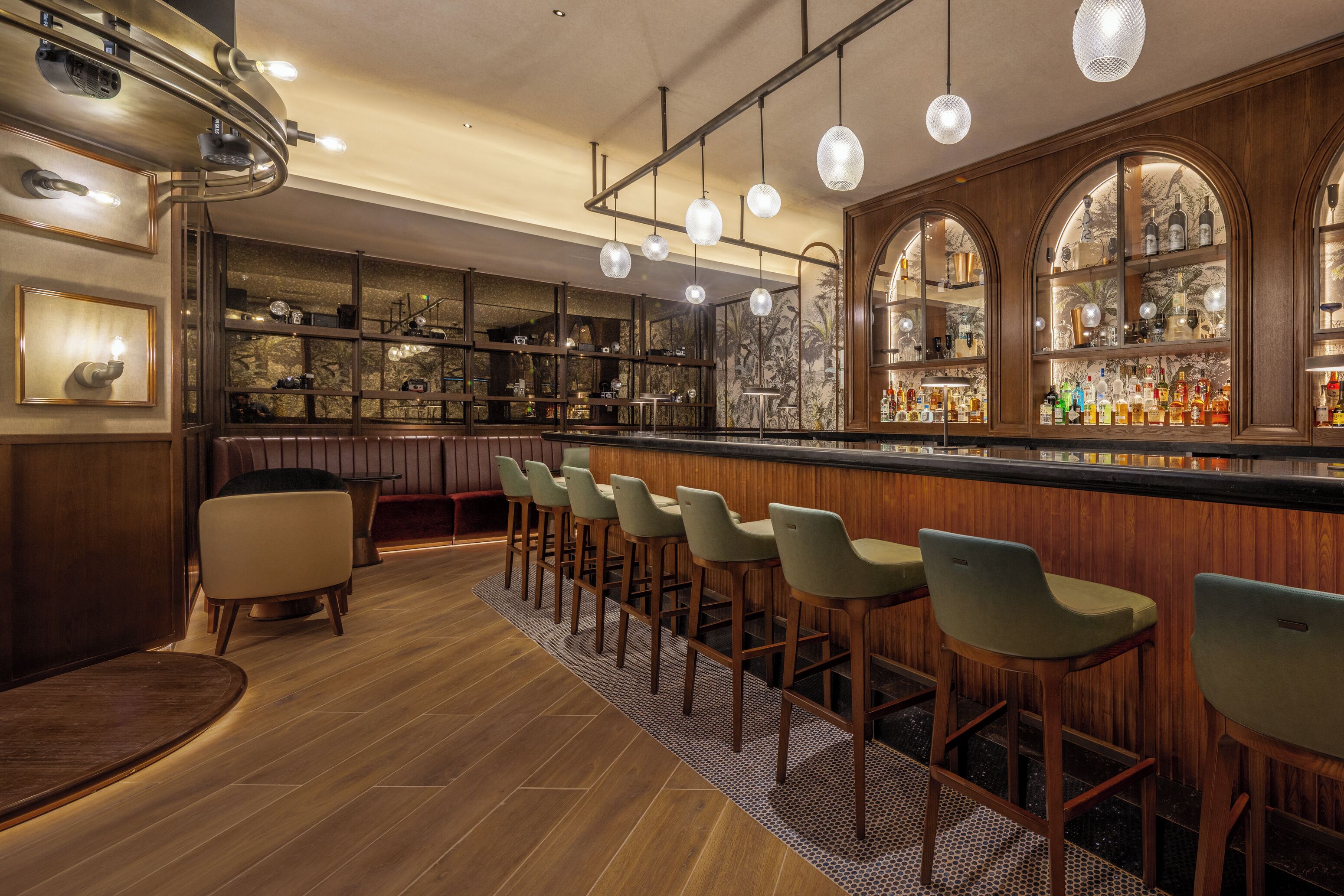 Een bar met houten barkrukken, een toonbank vol flessen en een behang met een patroon.