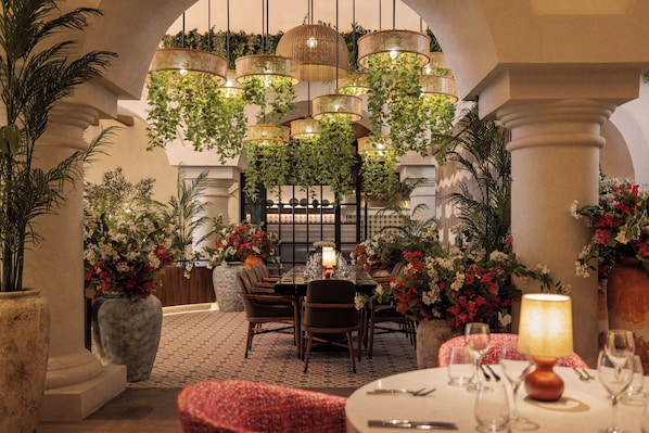 A dining area with a table set for four, surrounded by chairs, with hanging plants and a patterned floor.