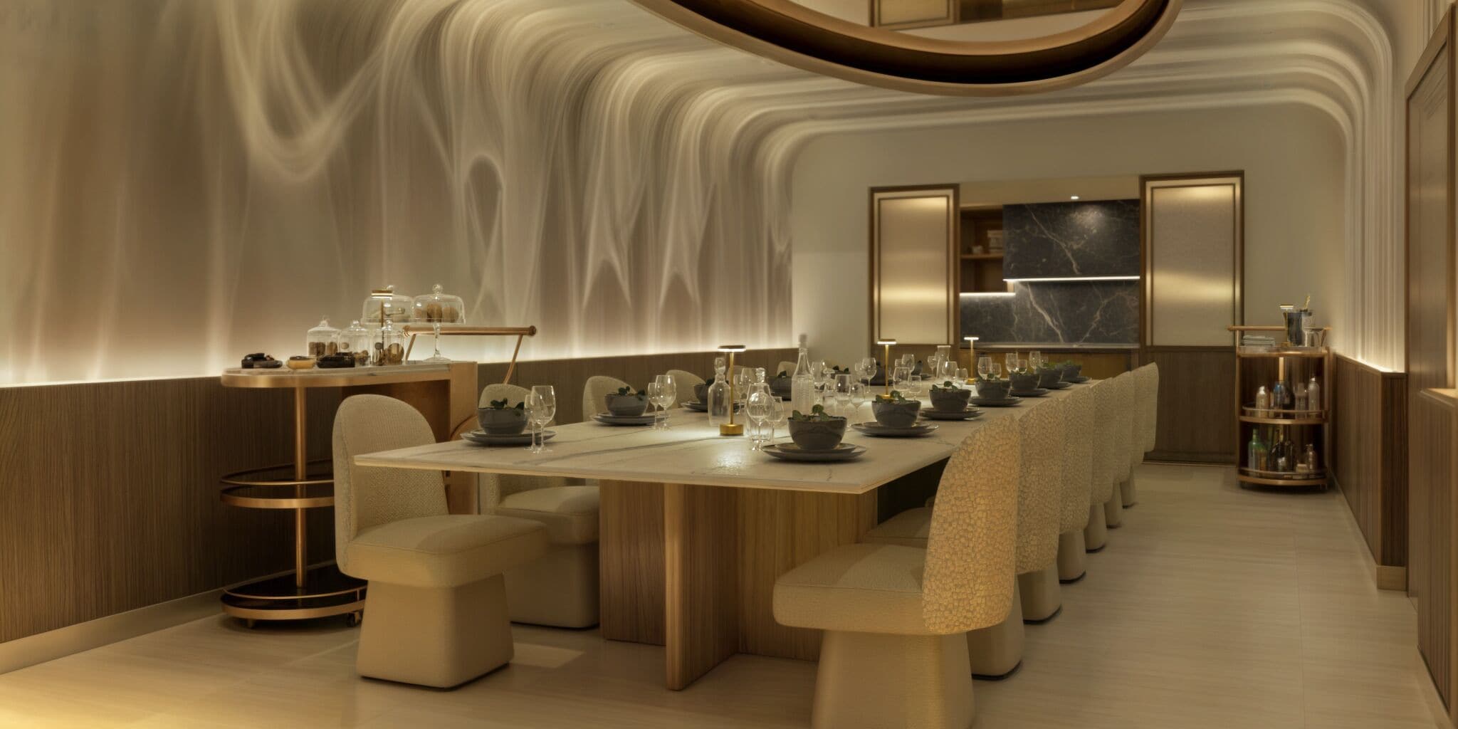 A modern dining area with a long table set for multiple guests, featuring a central light fixture and a marble backsplash.