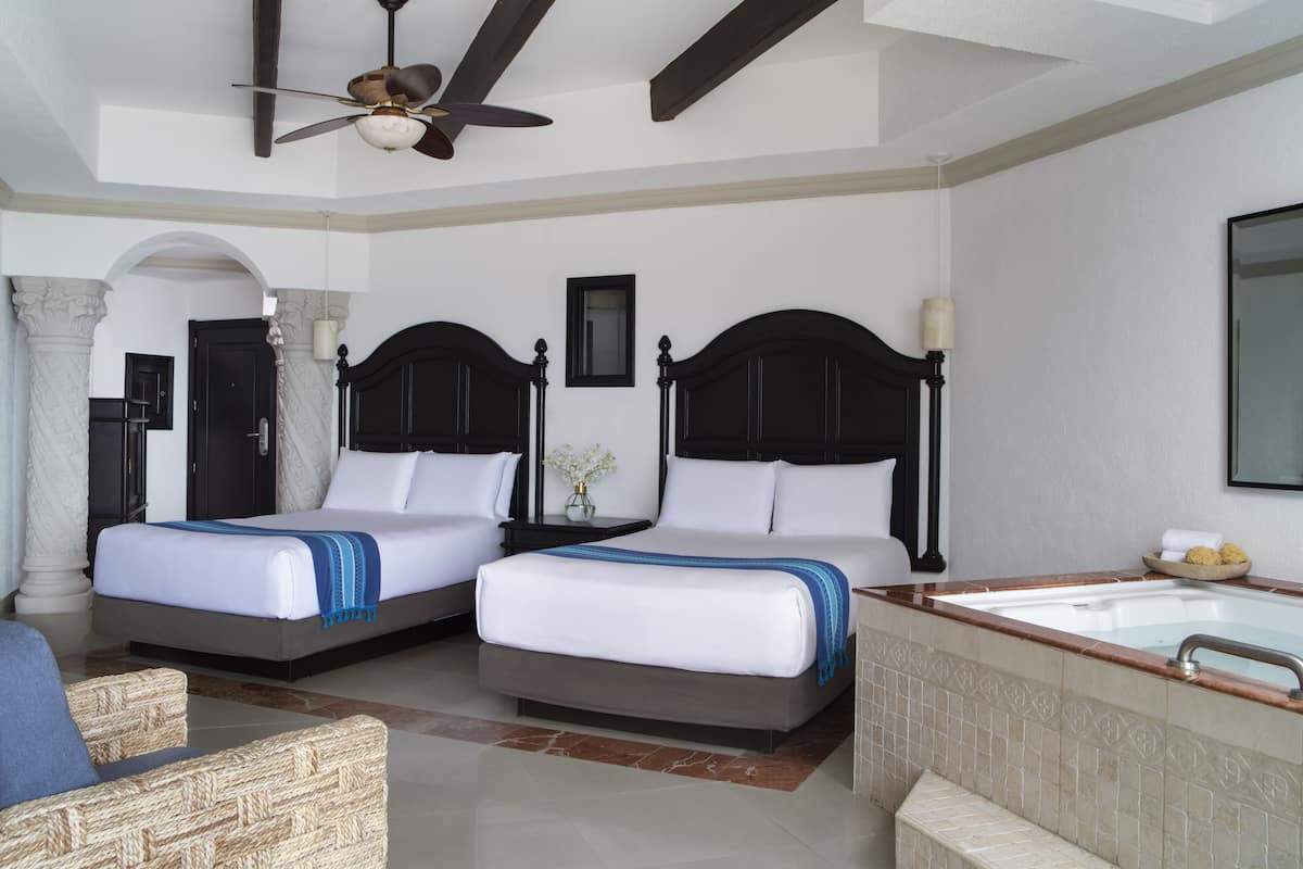 A hotel room with two beds, a sitting area, a bathtub, and a ceiling fan.