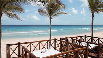 Una terraza de madera con una mesa y sillas que da a una playa con palmeras y el océano.