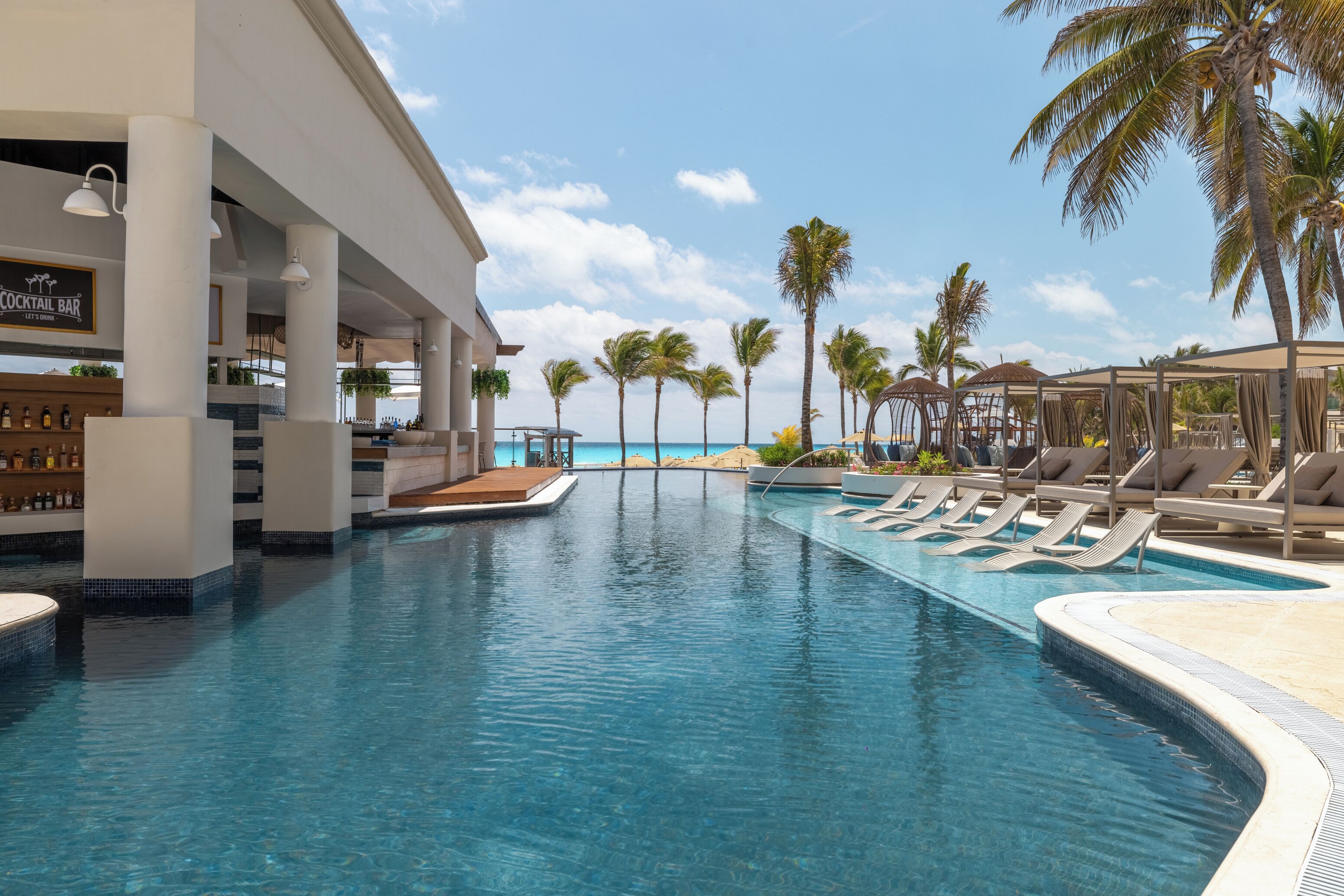 A pool area with lounge chairs, a bar, and palm trees.