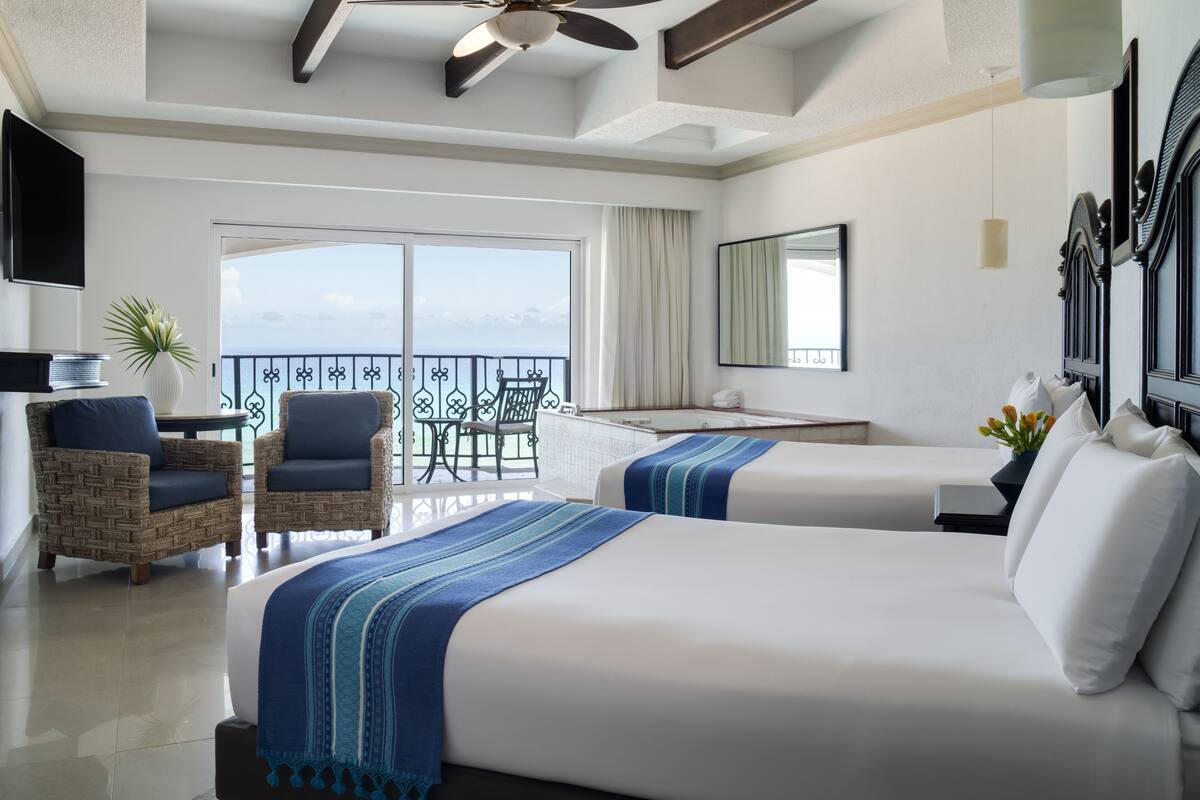 A hotel room with two beds, a balcony, a TV, and a ceiling fan.