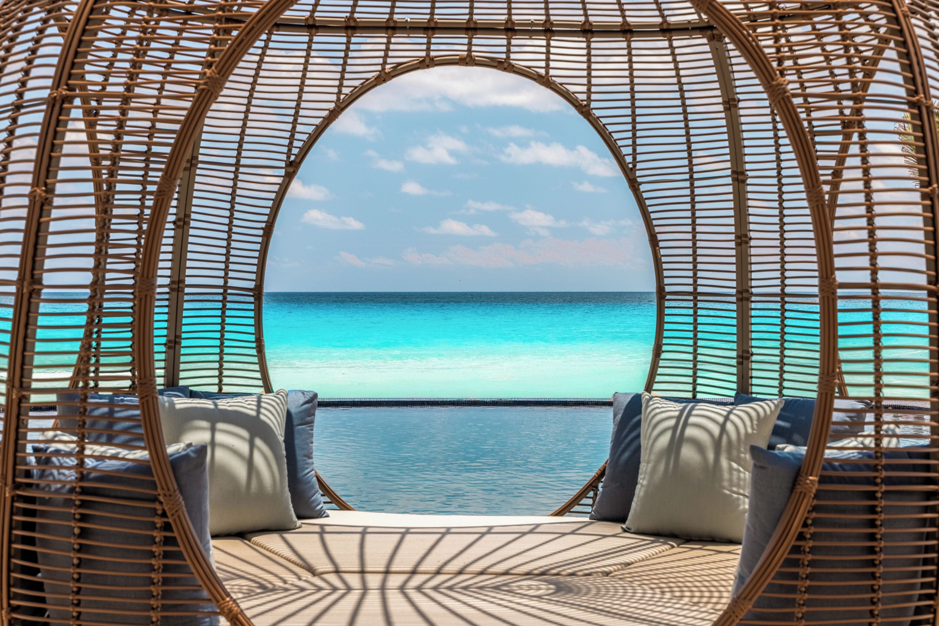 Un fauteuil rond en osier offrant une vue sur une mer turquoise et un ciel dégagé.
