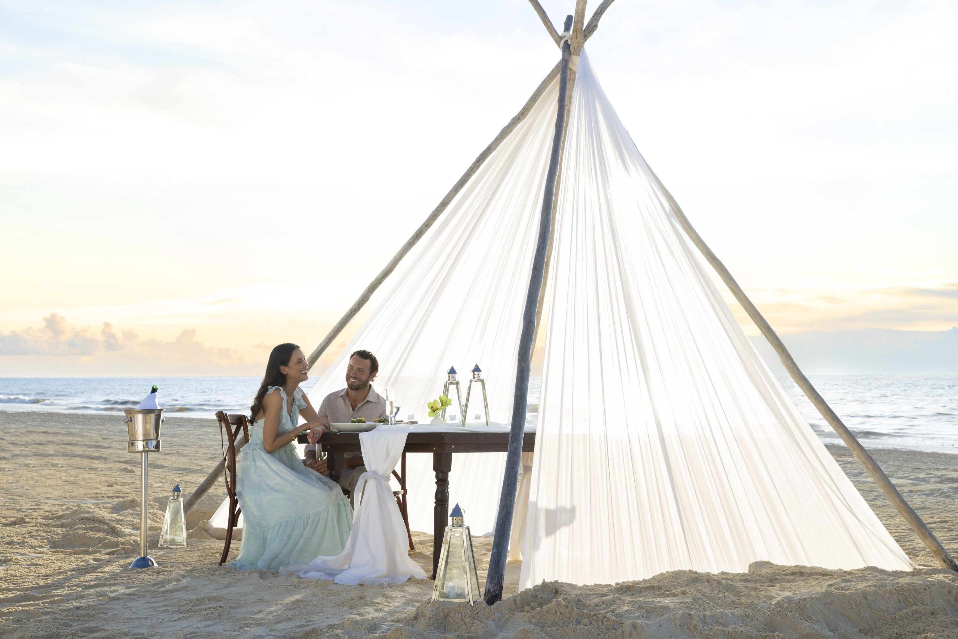 A tent on a beach with a table set for two.