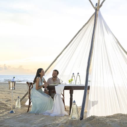 A tent on a beach with a table set for two.
