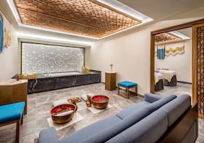 A modern spa room with a large seating area, a bathtub, and a wooden ceiling design.
