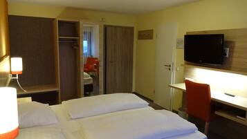 Een hotelkamer met een bed, bureau, stoel, televisie en een kledingkast.