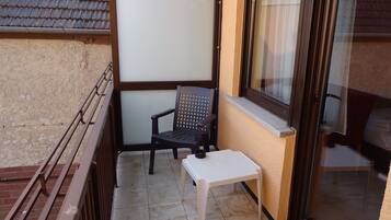 A small balcony with a chair, a small table, and a window with a curtain.
