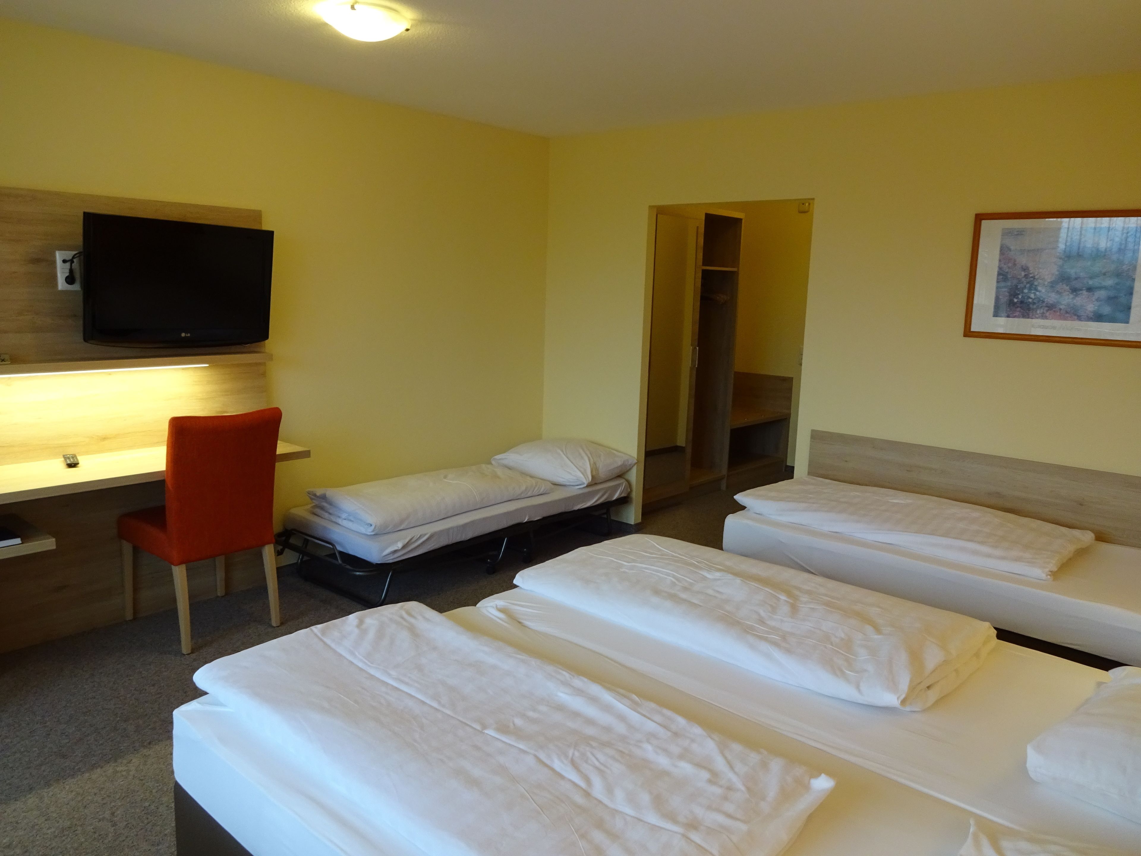Ein Hotelzimmer mit zwei Einzelbetten, einem Schreibtisch mit Stuhl, einem Fernseher und einem Bild an der Wand.