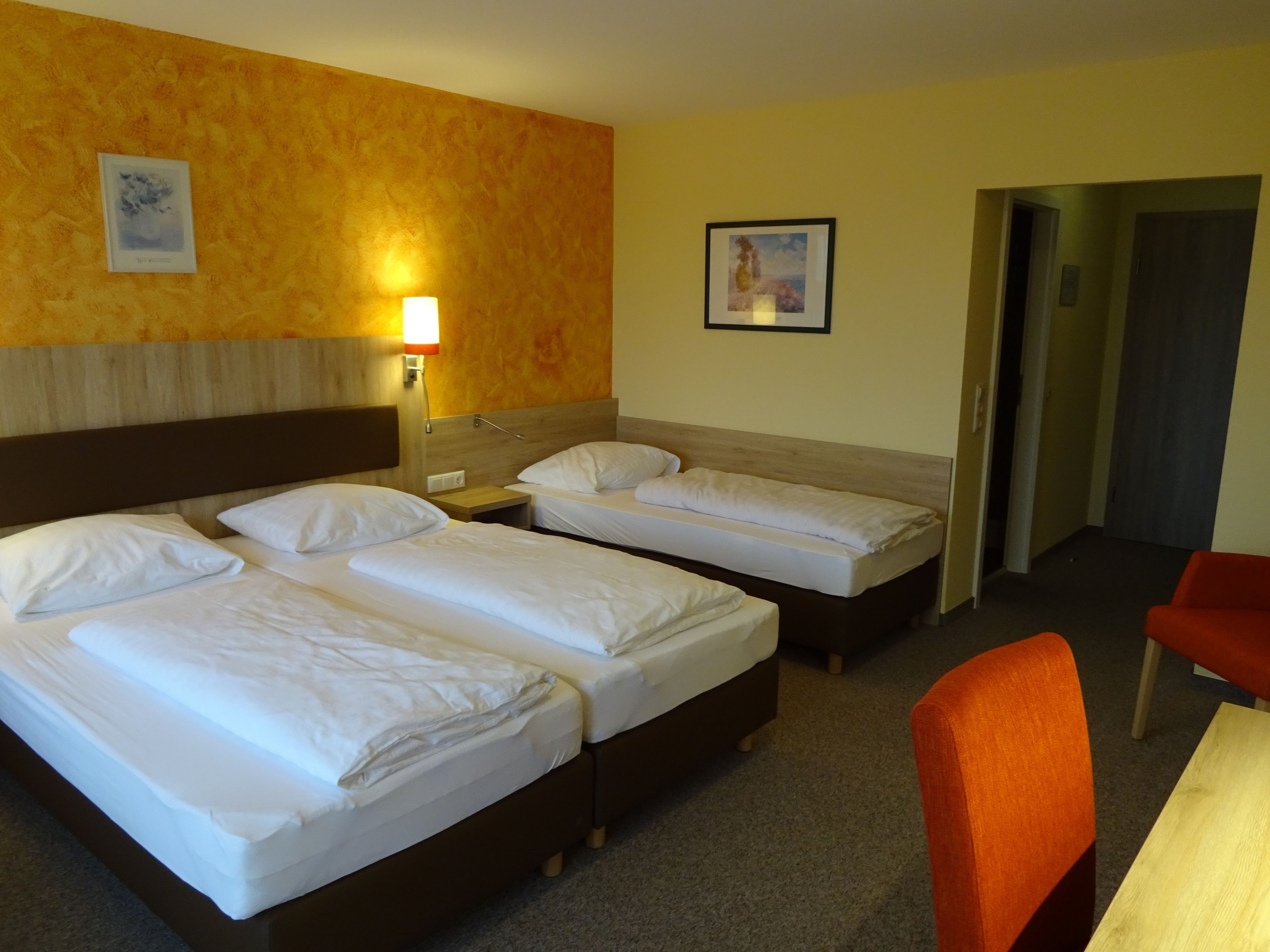 A hotel room with two single beds, a wooden headboard, a nightstand with a lamp, and a framed picture on the wall.