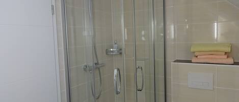A glass-enclosed shower with a handheld showerhead and a wall-mounted faucet.
