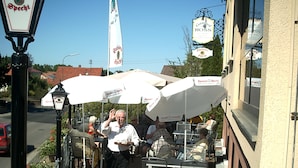 An outdoor seating area with tables and umbrellas, a street lamp, and a building with signage. - Gasthof Hotel Zum Ross (Wertheim)