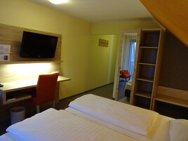 Una habitación de hotel con cama, escritorio, silla, televisor y armario.