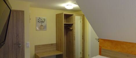 A bedroom with a bed, a wooden bench, a wardrobe, and a mirror.
