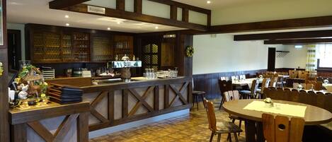 A restaurant with a reception area, wooden bar, tiled floor, and multiple dining tables.