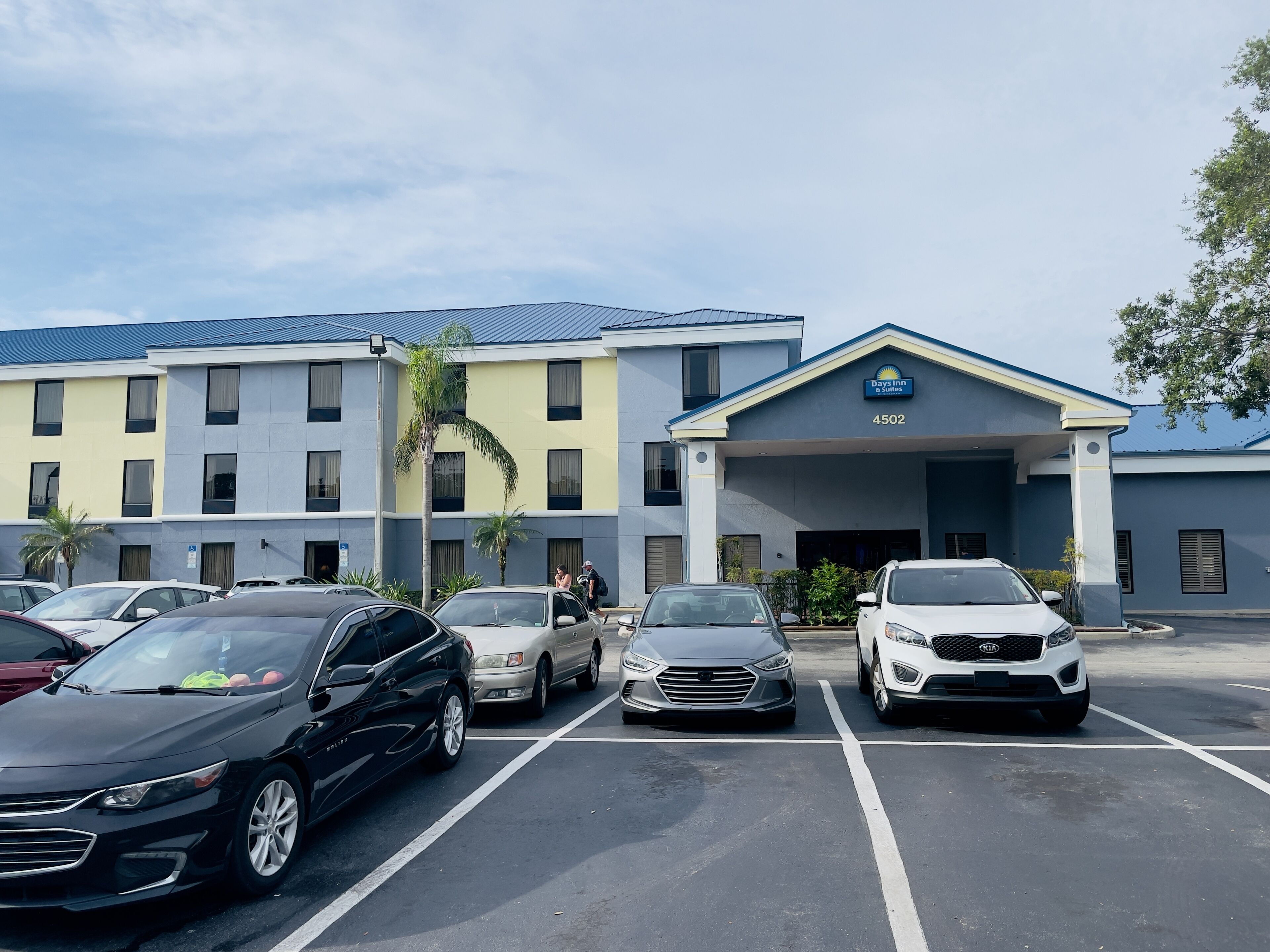 A hotel with a parking lot, multiple cars, and a building with a sign that reads "Days Inn & Suites."