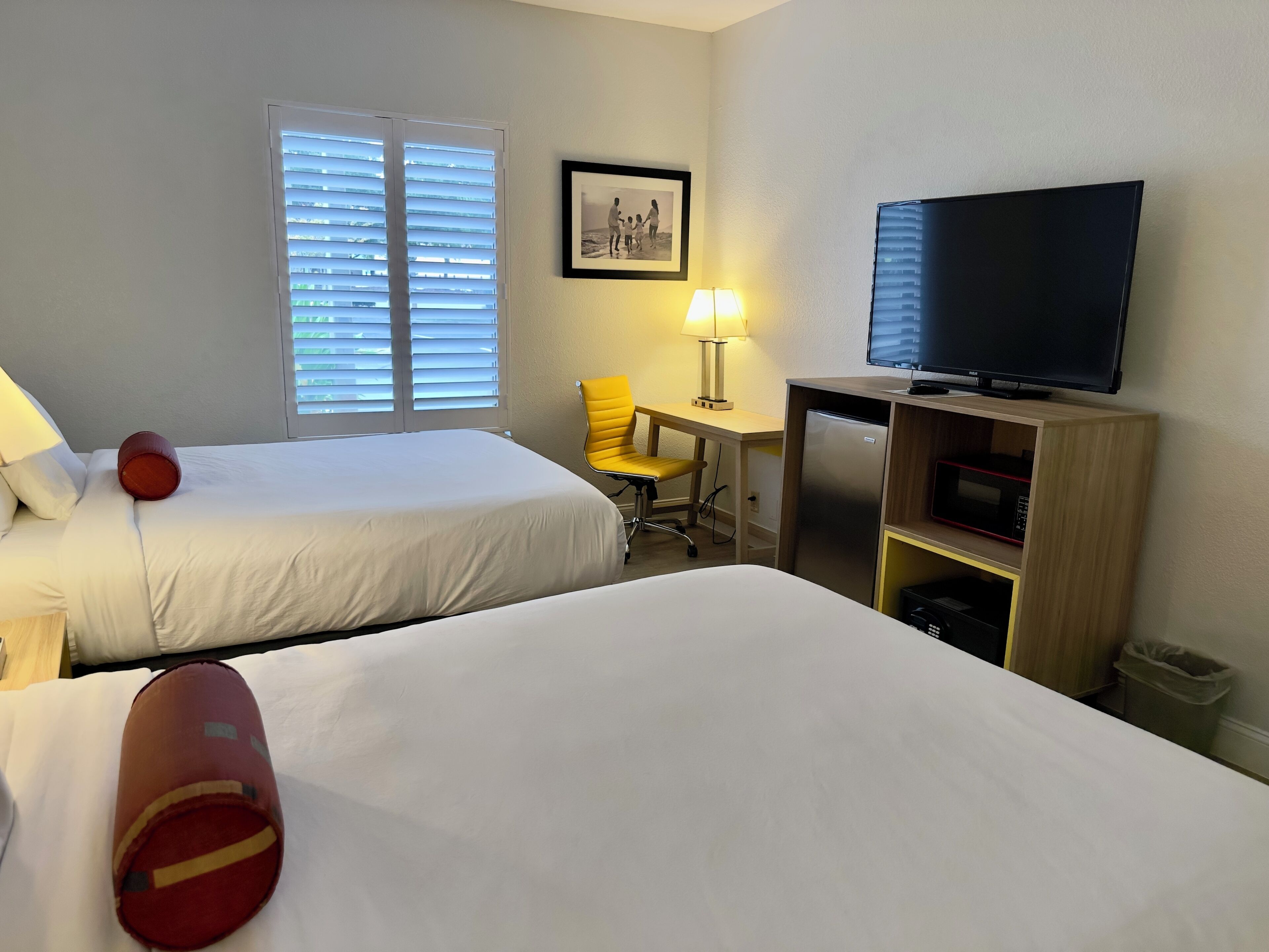 A hotel room with two beds, a desk with a lamp, a television, and a picture on the wall.