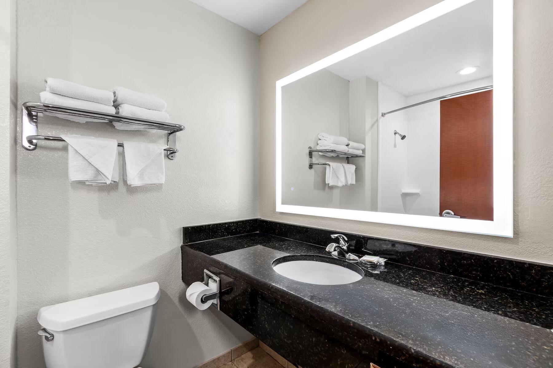 Ein modernes Badezimmer mit einem schwarzen Marmorwaschbecken, einer Toilette und einem Handtuchhalter mit gefalteten Handtüchern.