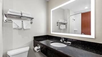 A modern bathroom with a black marble sink, a toilet, and a towel rack with folded towels.